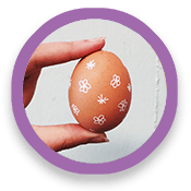 circle-waxresist1 Hand holds egg decorated with drawings of flowers and stars.
